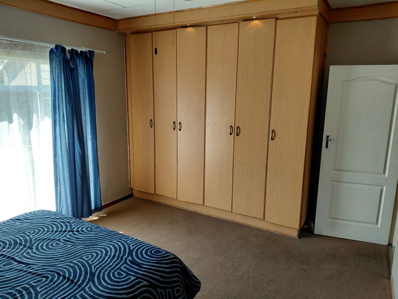 A bedroom featuring extensive light wood built-in cupboards with integrated lighting and carpeted flooring.