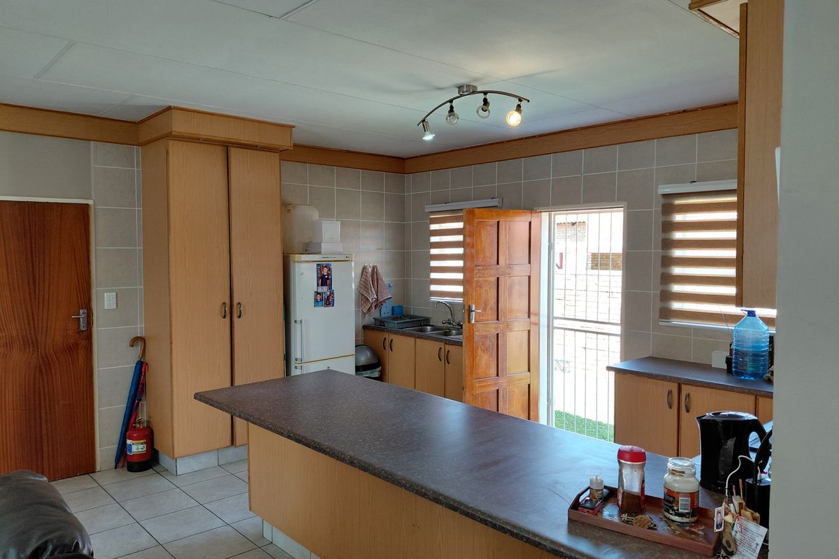 A functional kitchen featuring built-in wooden cabinetry, laminate countertops, tiled backsplash, and direct access to the exterior via a security gate.