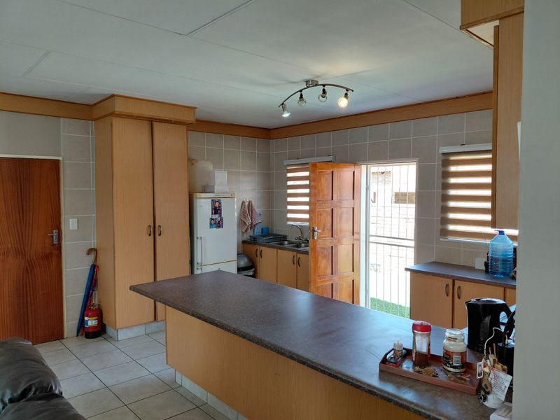A functional kitchen featuring built-in wooden cabinetry, laminate countertops, tiled backsplash, and direct access to the exterior via a security gate.