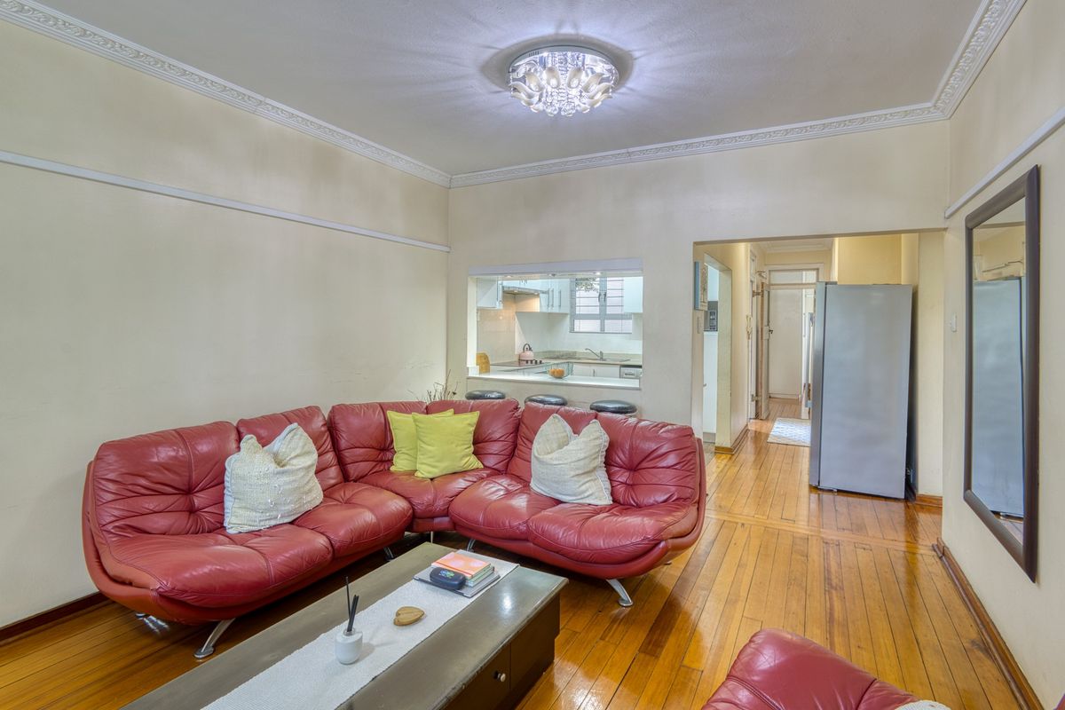 A living room featuring hardwood flooring, decorative ceiling cornicing, and a convenient pass-through window connecting to the kitchen area.