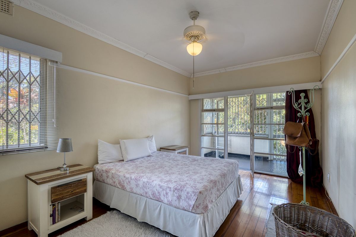 A bedroom featuring hardwood flooring, a ceiling fan, and direct access to a private balcony through a secure door.