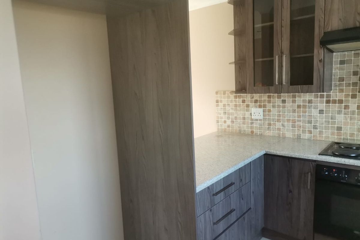 A clean, modern kitchen featuring dark wood-grain cabinetry, granite countertops, a mosaic tile backsplash, and integrated cooking appliances.