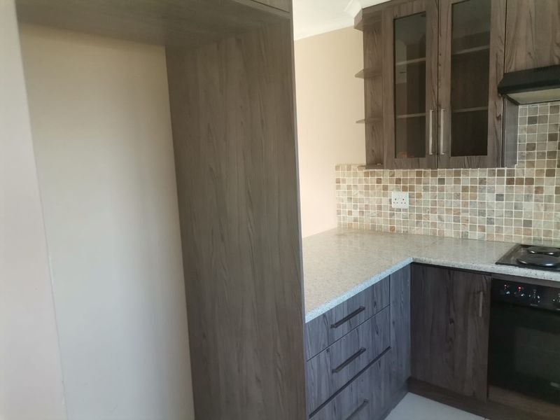 A clean, modern kitchen featuring dark wood-grain cabinetry, granite countertops, a mosaic tile backsplash, and integrated cooking appliances.