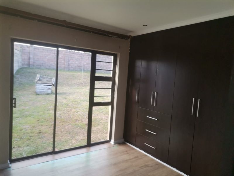 A bright bedroom featuring dark wood built-in cupboards, laminate flooring, and a sliding glass door providing direct access to the rear garden.