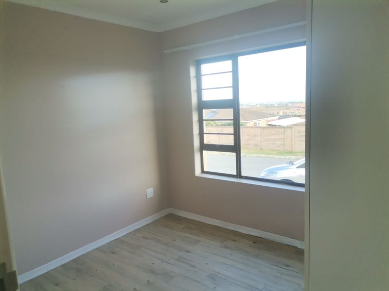 A bright, empty bedroom featuring laminate flooring, neutral wall tones, and a large window with security bars overlooking the street.