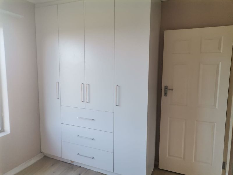 A clean bedroom featuring a modern white built-in wardrobe with integrated drawers and a classic panel door.