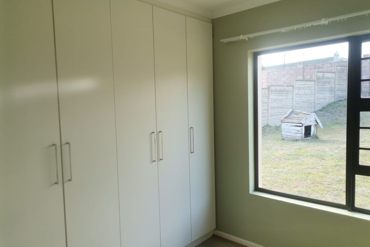 A bright, empty bedroom featuring floor-to-ceiling built-in cupboards, neutral green walls, and a large window overlooking the rear garden area.