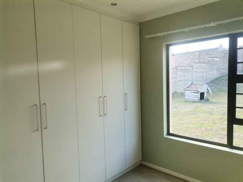 A bright, empty bedroom featuring floor-to-ceiling built-in cupboards, neutral green walls, and a large window overlooking the rear garden area.