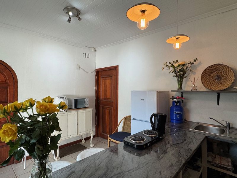 A compact kitchen area featuring stone countertops, a stainless steel sink, and classic timber doors, illuminated by modern pendant lighting.
