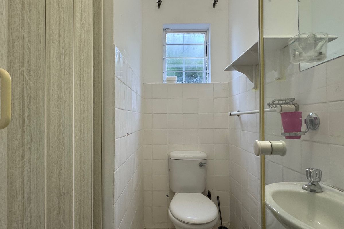 A compact bathroom featuring a toilet, wall-mounted basin, and glass shower screen, finished with white wall tiles and security bars on the window.