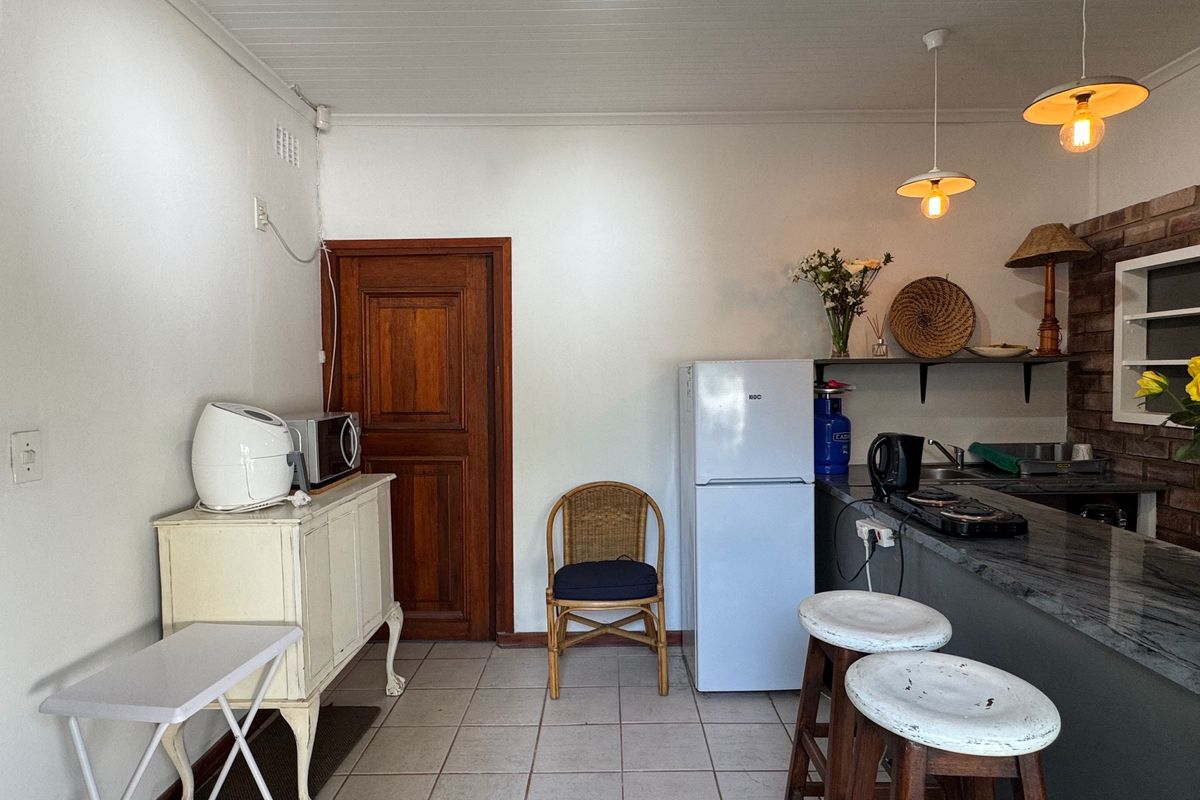A functional kitchen area featuring a stone-topped breakfast bar, pendant lighting, tiled flooring, and a classic timber door, offering a practical layout.