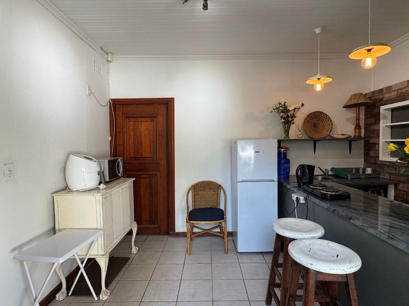 A functional kitchen area featuring a stone-topped breakfast bar, pendant lighting, tiled flooring, and a classic timber door, offering a practical layout.
