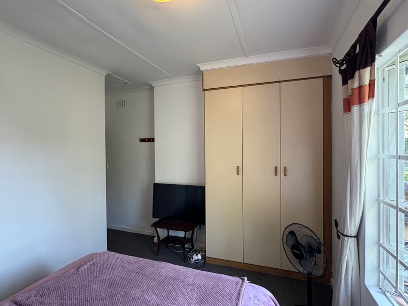 A functional bedroom featuring a built-in wardrobe, carpeted flooring, and a window with security bars, offering a neutral base for potential updates.