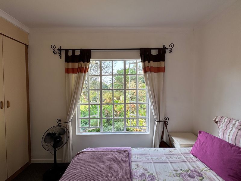 A cozy bedroom featuring a large lattice window with garden views and a built-in wardrobe, offering a bright and peaceful atmosphere.