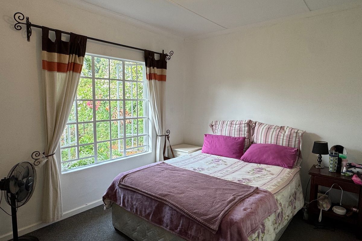 A functional bedroom featuring a large window with security bars, neutral wall finishes, and carpeted flooring.