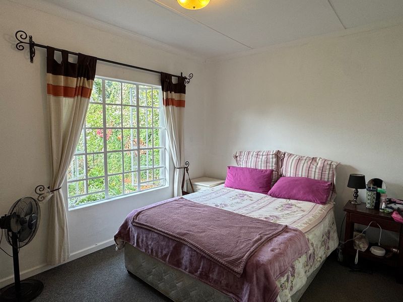 A functional bedroom featuring a large window with security bars, neutral wall finishes, and carpeted flooring.
