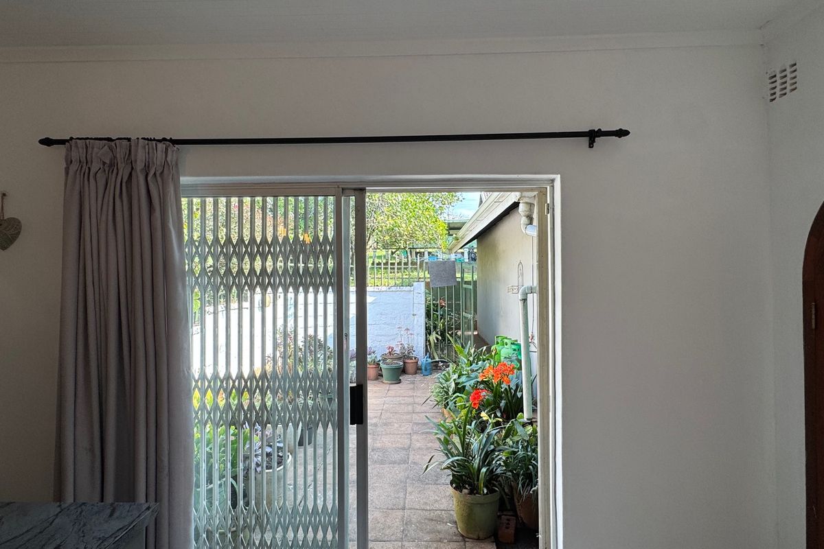 A bright living area featuring a sliding glass door with a security gate, providing direct access to the rear patio and garden.