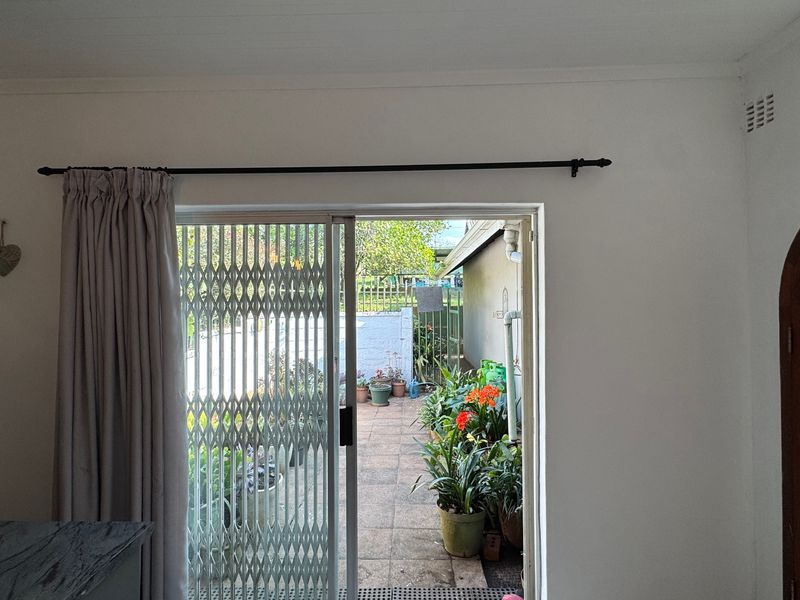 A bright living area featuring a sliding glass door with a security gate, providing direct access to the rear patio and garden.