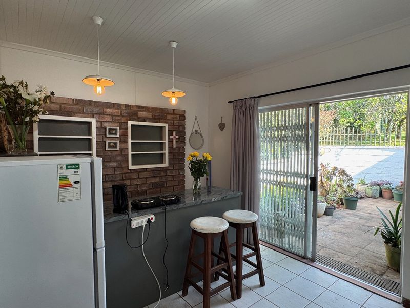 A cozy kitchen area featuring an exposed brick wall, breakfast bar, and direct access to a paved outdoor patio through sliding glass doors.