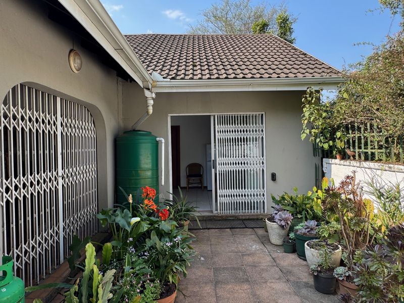 A rear patio area featuring tiled flooring, sliding security gates, and a water storage tank, set against the cottage exterior.