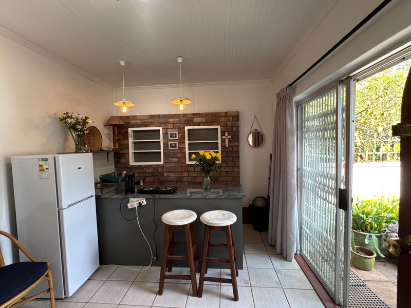 A compact kitchen area featuring an exposed brick backsplash, stone countertop, and direct access to an outdoor patio through sliding glass doors.