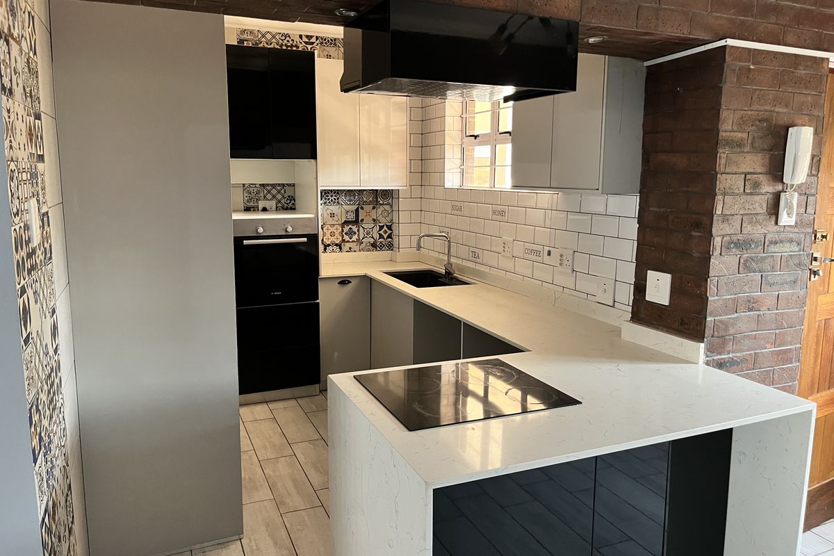 Modern kitchen featuring quartz countertops, subway tile backsplash, built-in oven, electric hob, and a unique exposed brick accent wall.