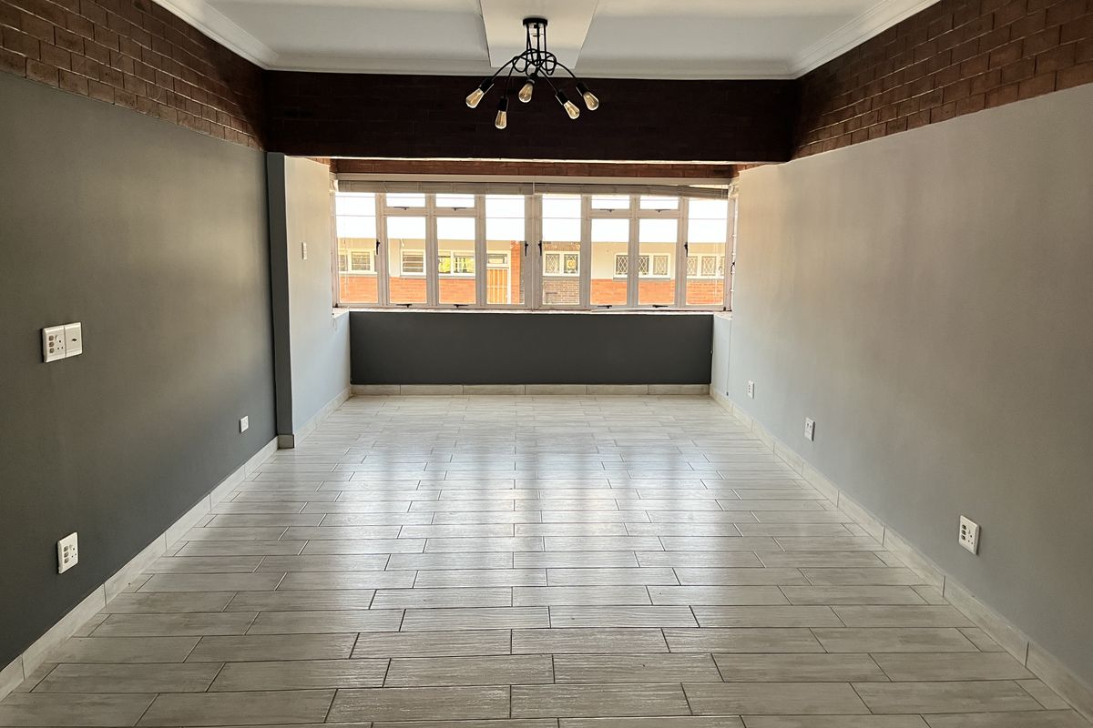 A bright, empty living room featuring modern tiled flooring, exposed brick accents, and a unique recessed ceiling design with contemporary lighting.