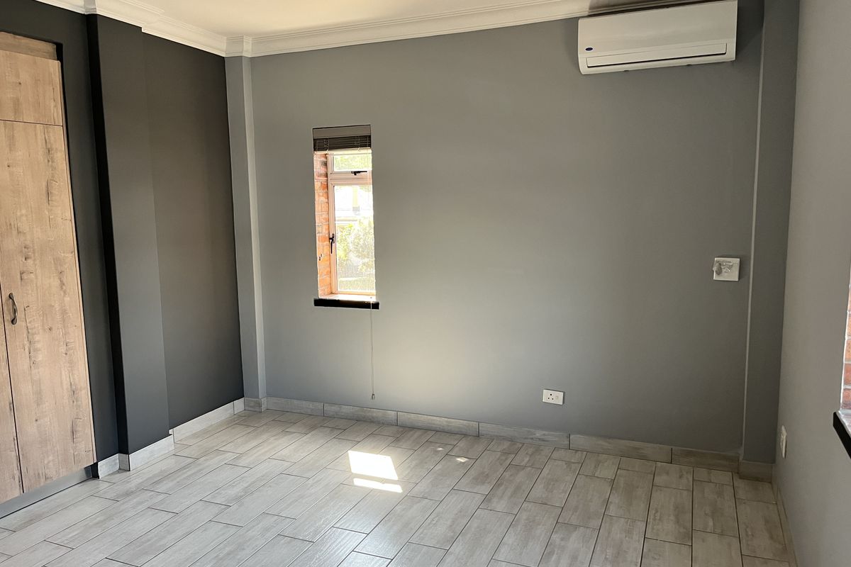A clean, empty bedroom featuring modern grey walls, wood-look tiled flooring, built-in cupboards, and a wall-mounted air conditioning unit.