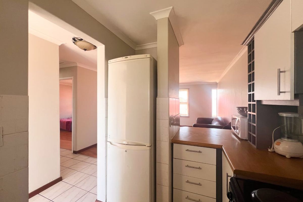 A functional kitchen area featuring built-in cabinetry, laminate countertops, and tiled flooring, with an open-plan layout connecting to the living space.