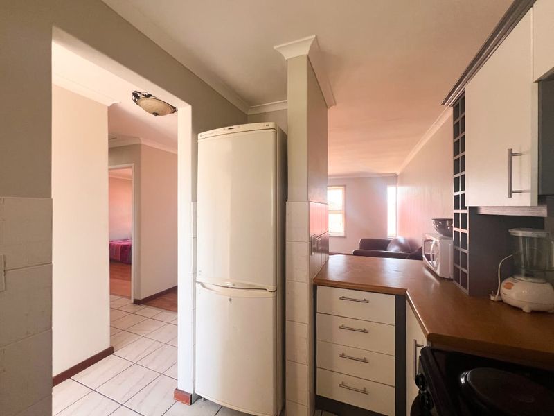 A functional kitchen area featuring built-in cabinetry, laminate countertops, and tiled flooring, with an open-plan layout connecting to the living space.