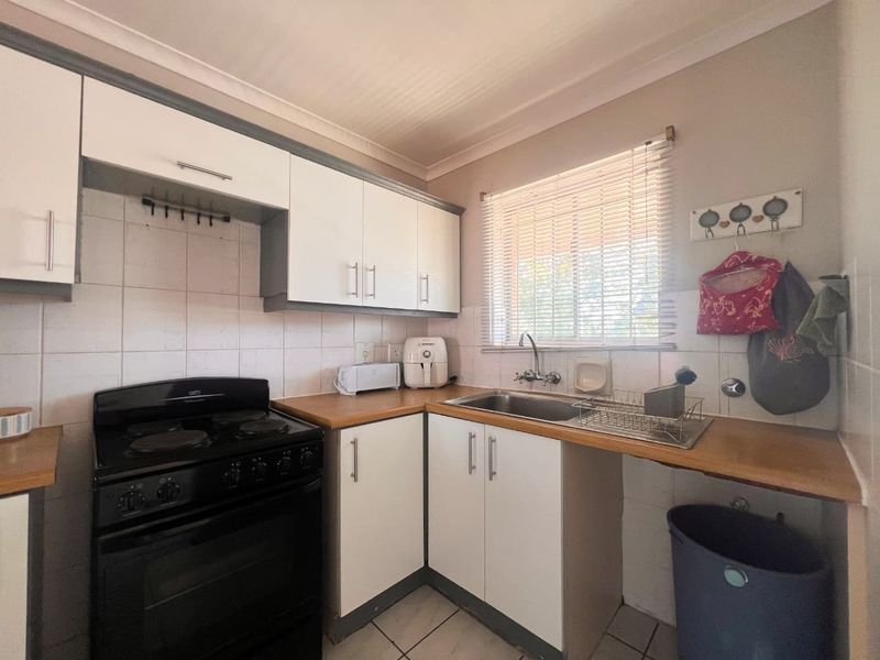 A functional kitchen featuring white cabinetry, laminate countertops, a tiled backsplash, and a freestanding stove, illuminated by natural light through a window with blinds.