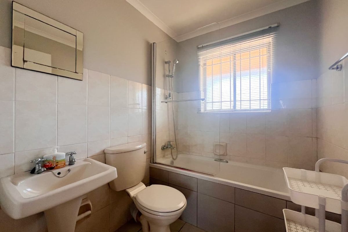 A functional bathroom featuring a pedestal basin, toilet, and a bathtub with a glass shower screen and tiled finishes.