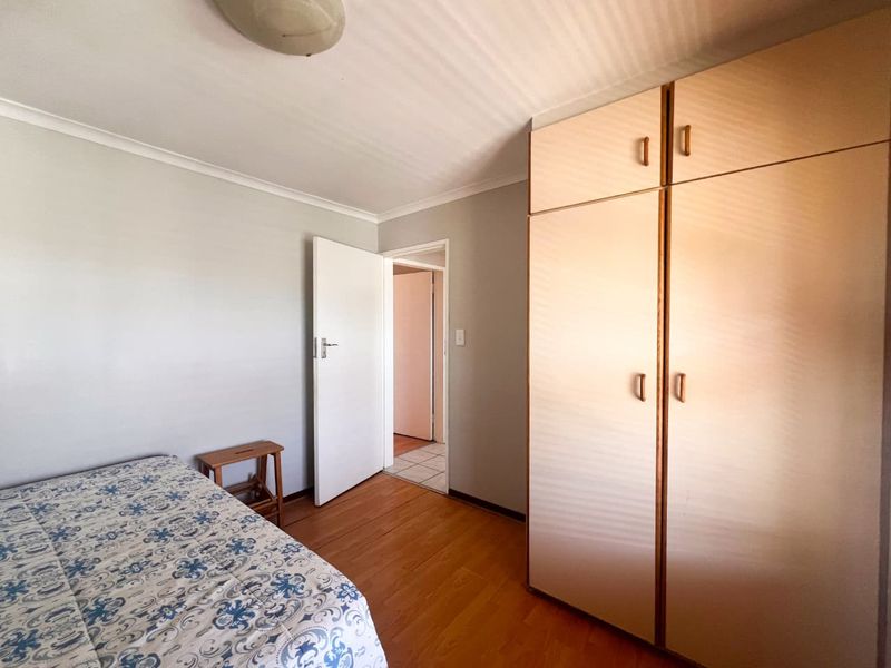 A bedroom featuring laminate flooring, coved ceilings, and built-in cupboards, providing functional storage space.