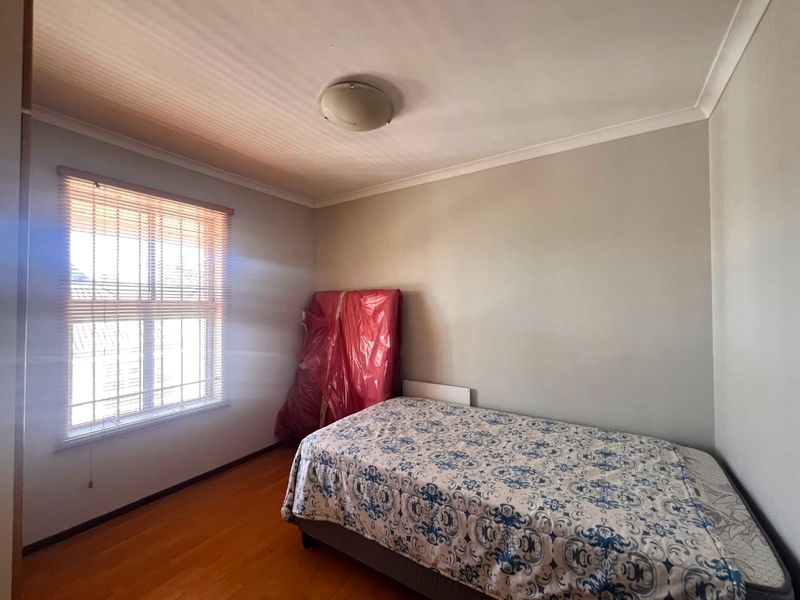 A functional bedroom featuring laminate flooring, a window with security bars, and a simple ceiling light fixture.