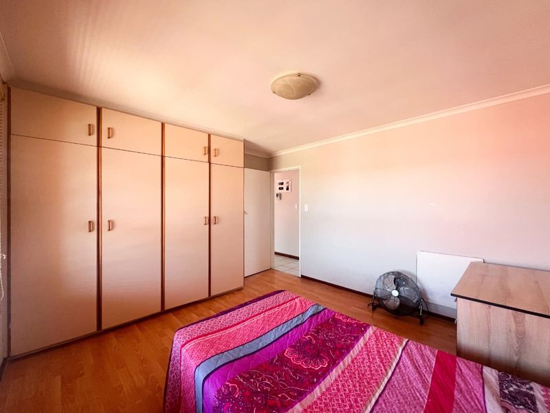 A bedroom featuring laminate flooring and extensive built-in cupboard storage, offering a functional space with neutral wall finishes.