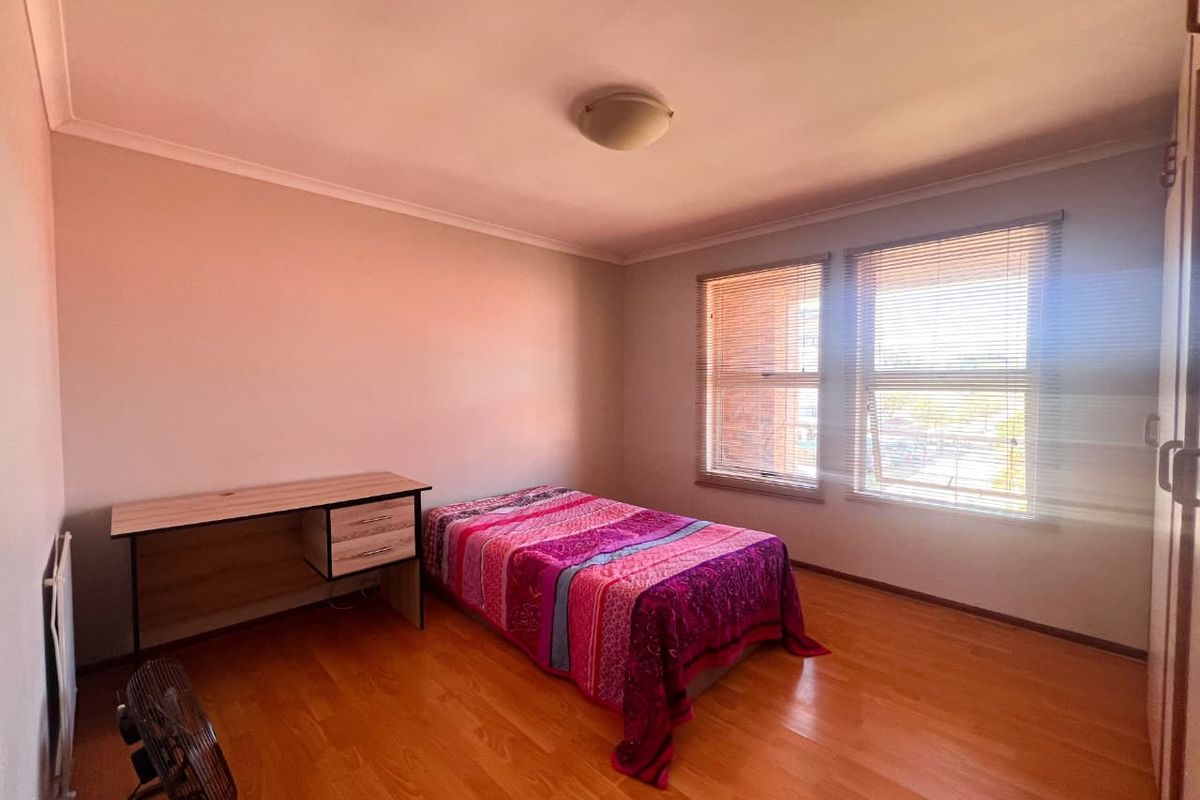 A functional bedroom featuring laminate flooring, built-in cupboards, and venetian blinds, offering a neutral space ready for personalization.