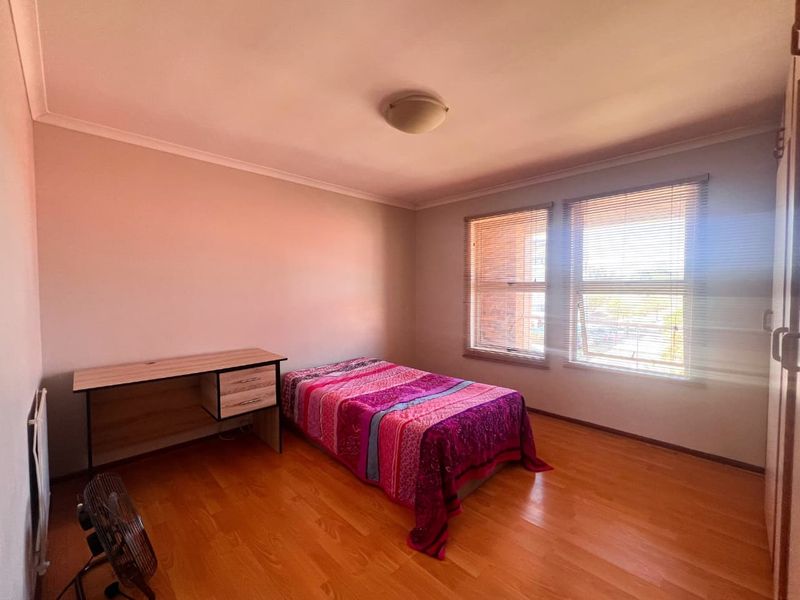 A functional bedroom featuring laminate flooring, built-in cupboards, and venetian blinds, offering a neutral space ready for personalization.