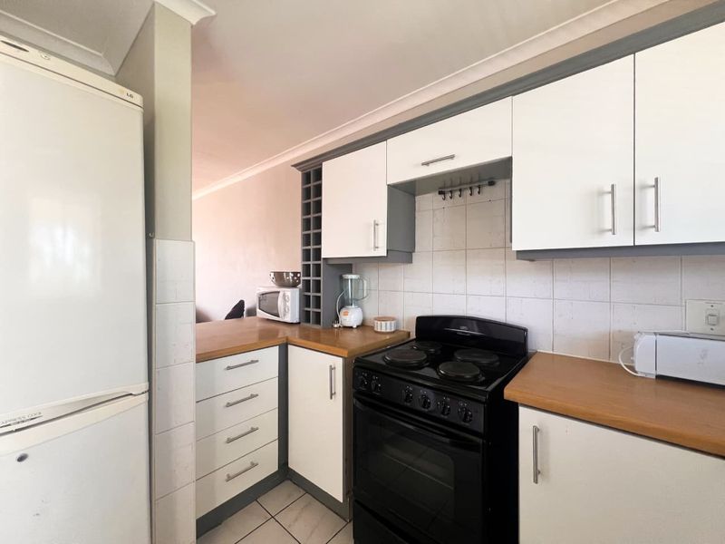 A functional kitchen featuring white cabinetry, wood-look laminate countertops, tiled backsplash, and a black stove, offering a clean and practical cooking space.