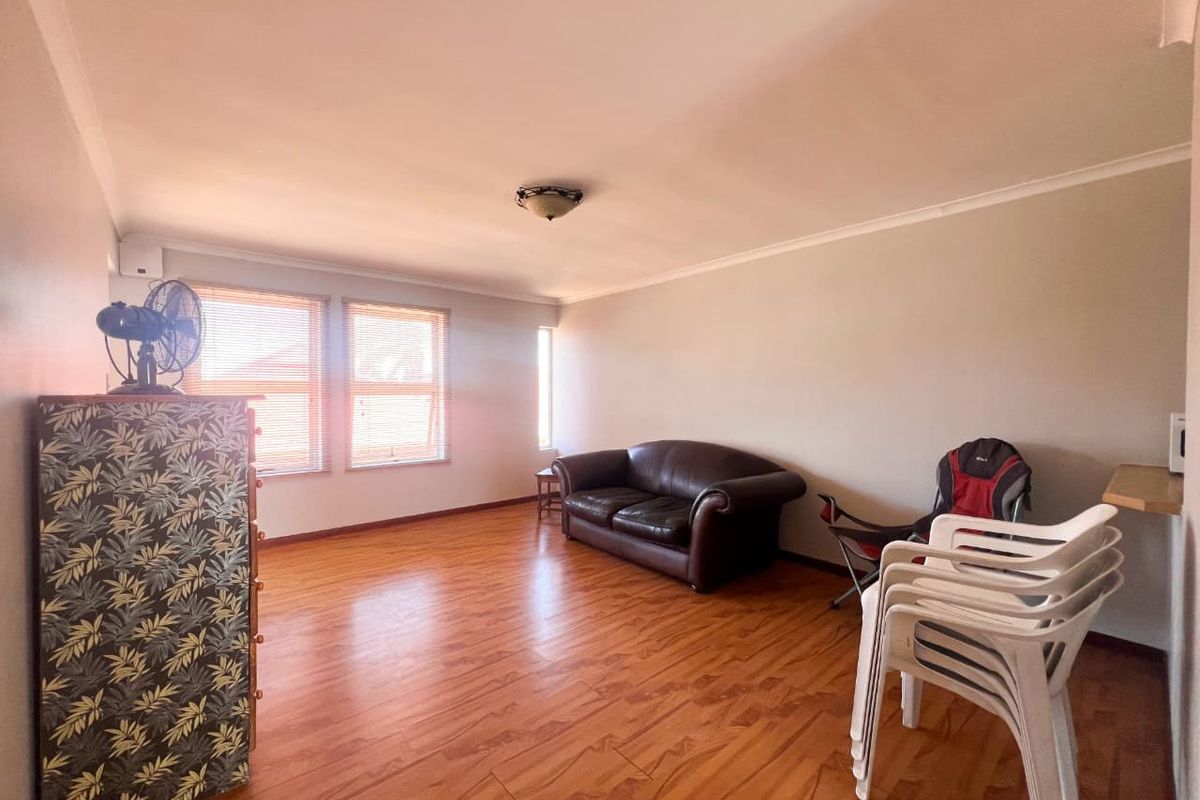 A spacious living room featuring laminate wood flooring, neutral walls, and natural light through venetian blinds.