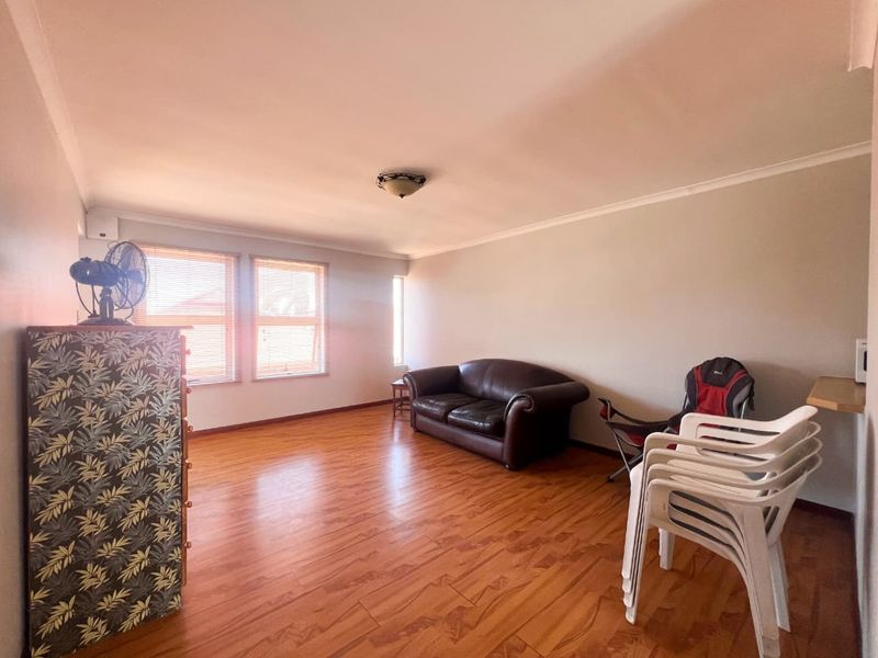 A spacious living room featuring laminate wood flooring, neutral walls, and natural light through venetian blinds.