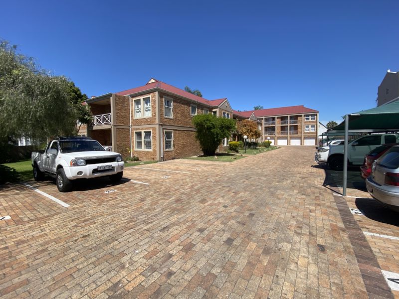 Exterior view of a multi-story brick apartment complex featuring a paved parking area, carports, and balcony access.