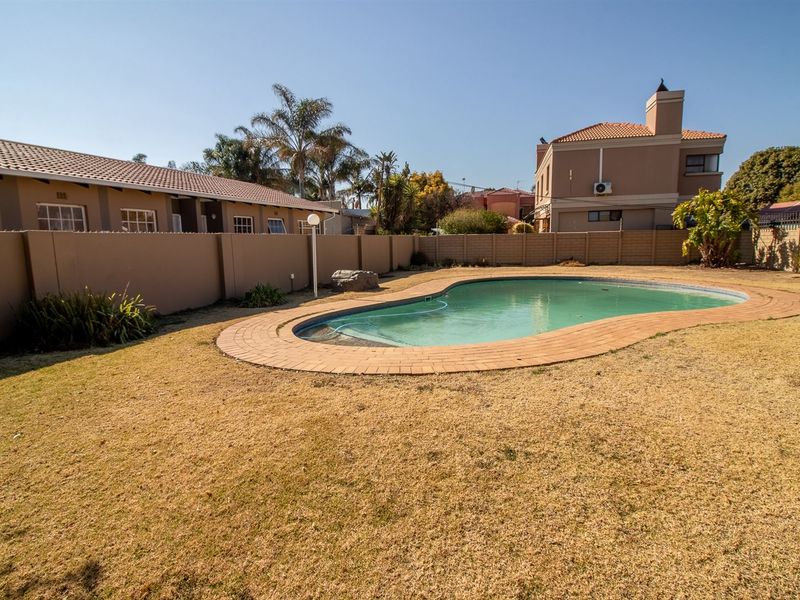 Outdoor pool area featuring a swimming pool with brick coping, surrounded by a lawn and perimeter boundary wall in a townhouse complex setting.