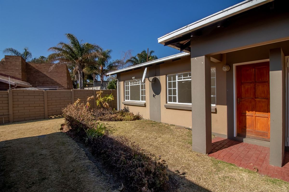 Rear exterior view of the townhouse featuring a small garden, brick boundary wall, and a covered entrance porch with a wooden door.