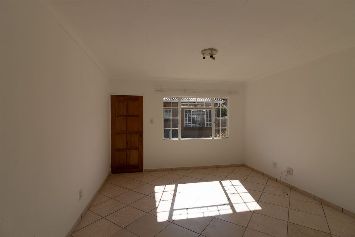 A bright, empty bedroom featuring neutral tiled flooring, a wooden door, and a multi-pane window allowing for natural light.