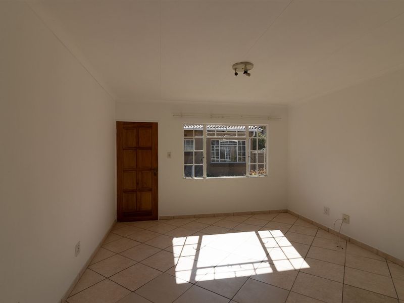 A bright, empty bedroom featuring neutral tiled flooring, a wooden door, and a multi-pane window allowing for natural light.