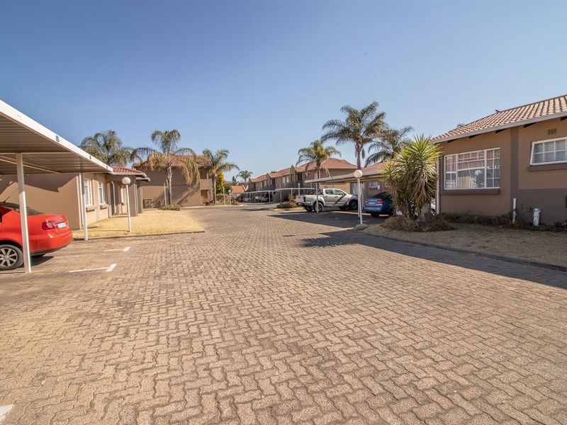 A view of the townhouse complex exterior featuring paved driveways, covered carports, and well-maintained building facades with tiled roofs.