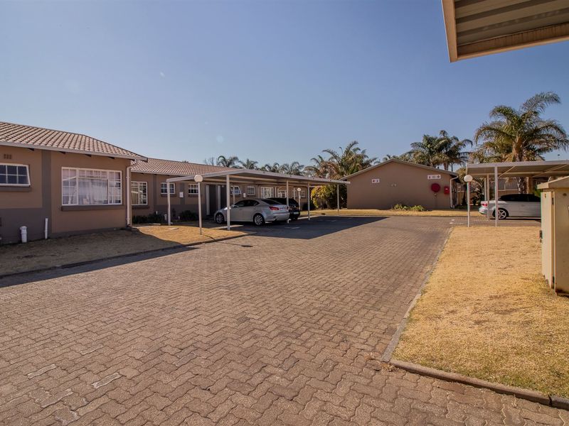 Exterior view of a townhouse complex featuring a paved driveway, covered carports, and well-maintained building facades.