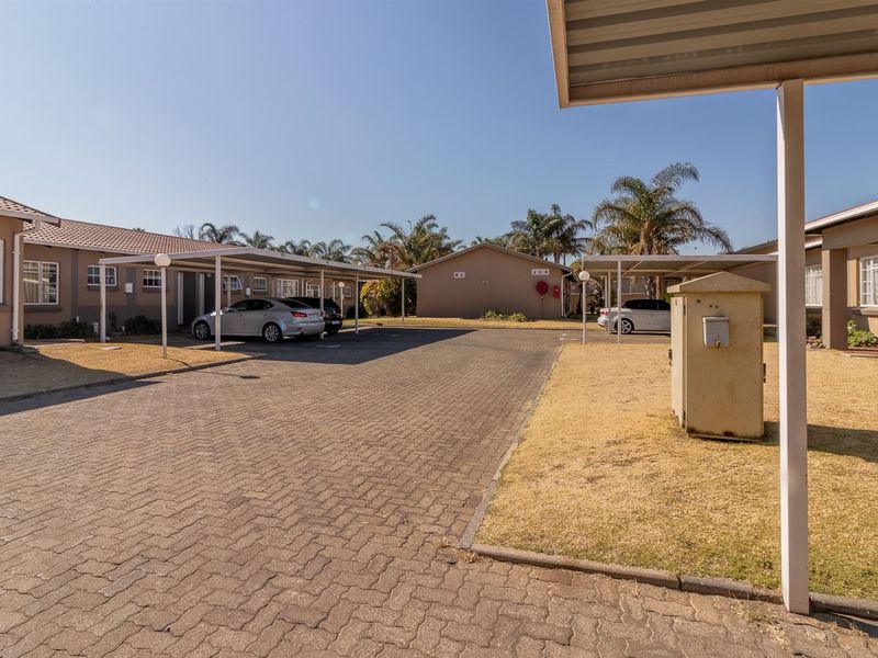 Exterior view of a townhouse complex featuring paved driveways, covered carports, and established landscaping.