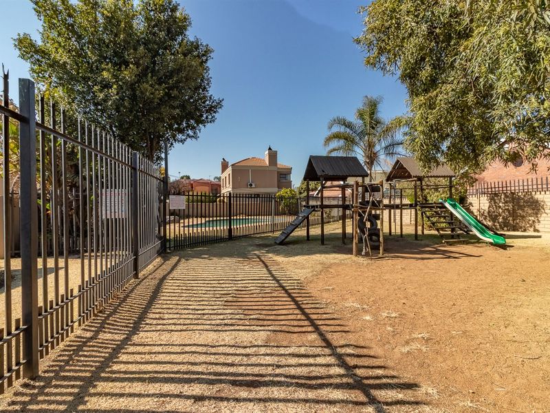 A communal outdoor area featuring a playground with climbing structures and slides, enclosed by metal fencing and brick boundary walls.