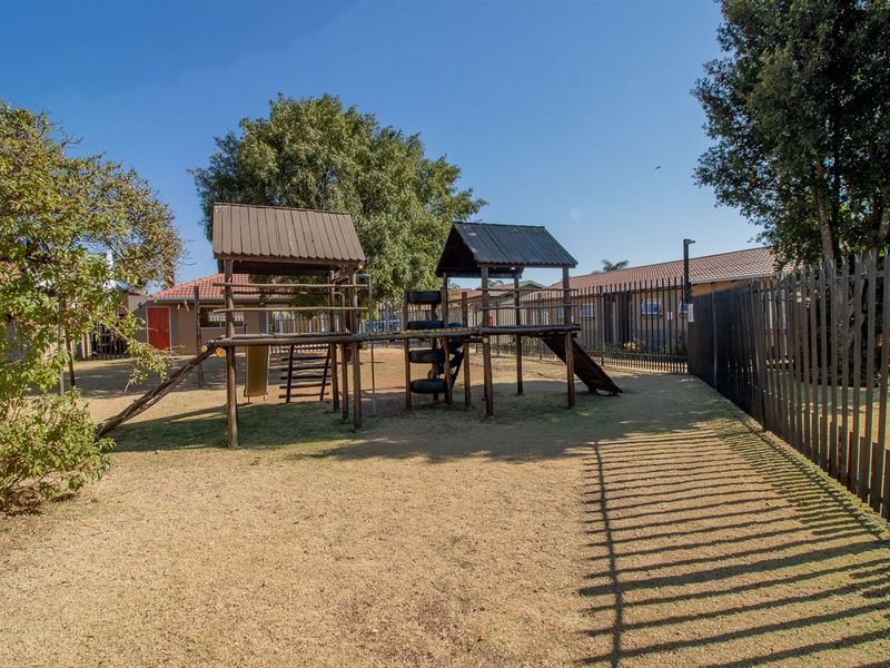 Communal outdoor playground area featuring wooden play structures and secure metal perimeter fencing within the townhouse complex.